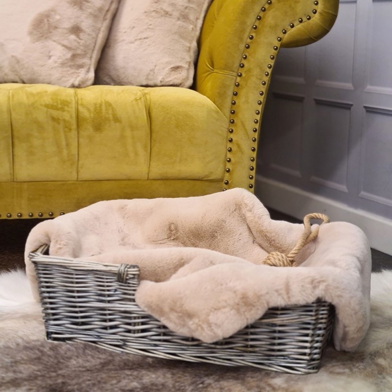 Chelsea Sandstone faux fur dog blanket in a wicker basket beside a mustard velvet sofa